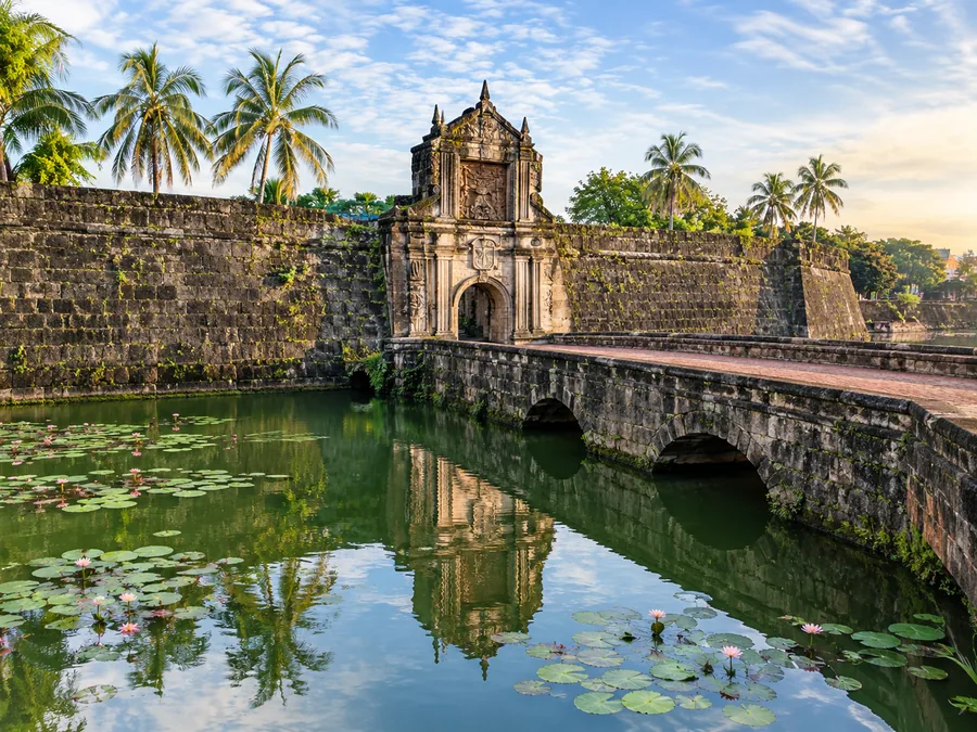 Der grüne Wassergraben unter den Mauern von Fort Santiago, mit Seerosenblättern und einer Steinbrücke zum Tor